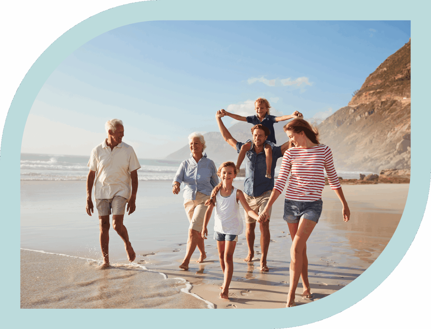 A joyful multigenerational family walks along the beach at sunset.