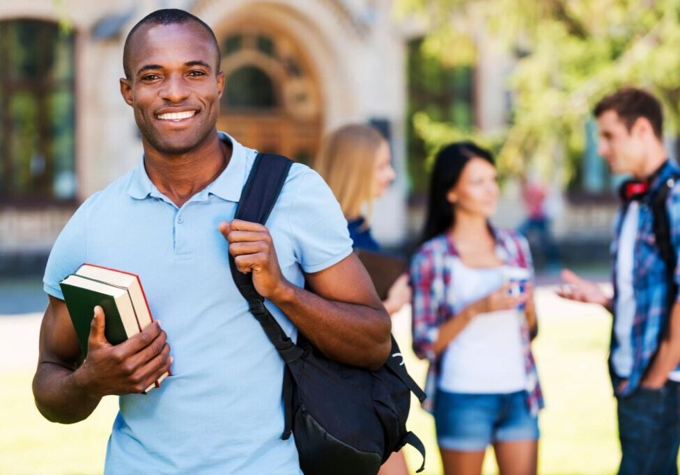 Student smiling with books and backpack outside.