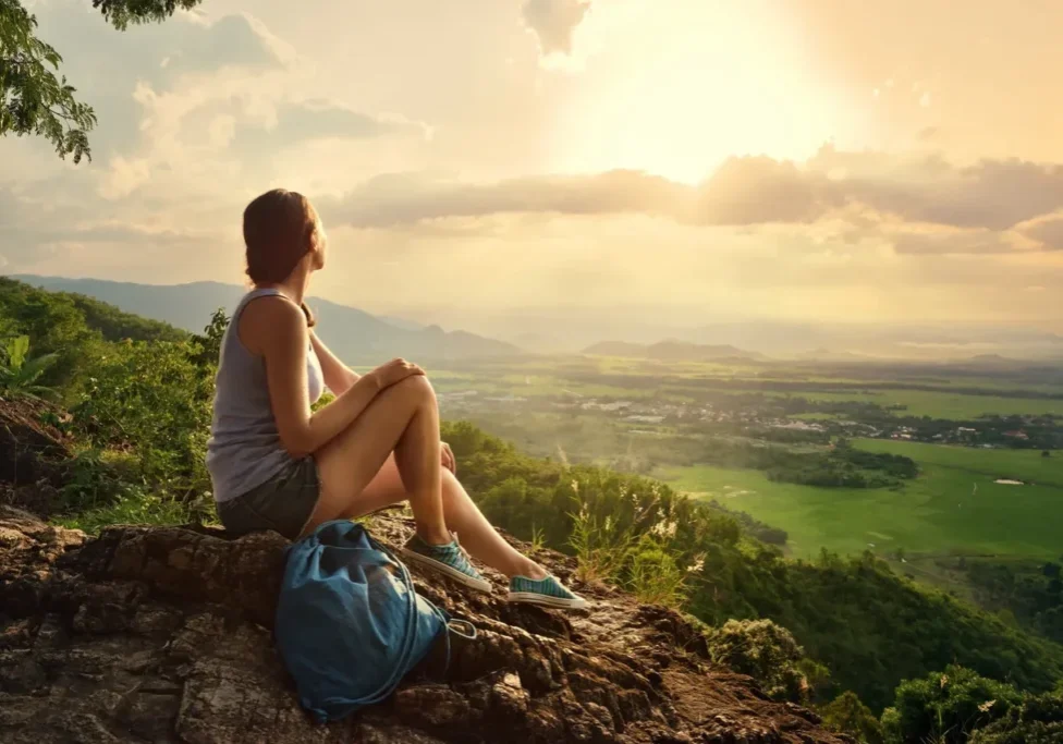 Person enjoying sunset view from a mountain top with a backpack.